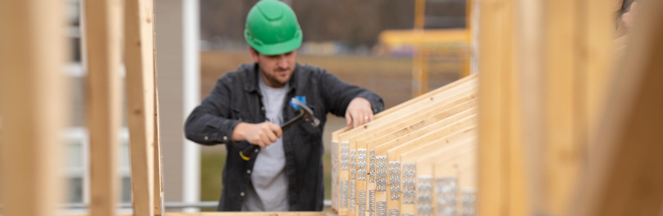 Guy in green hard hat hammering wood to build a house